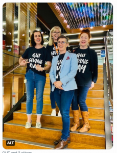 4 people wearing "QUT Giving Shirts" stand on the stairs at KG Library